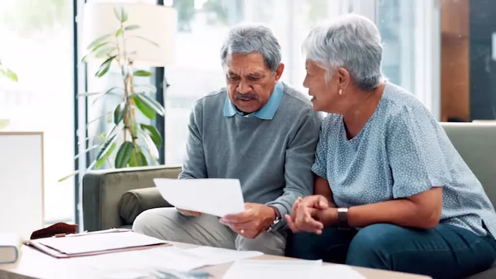 An older couple on their sofa, reviewing paperwork together.