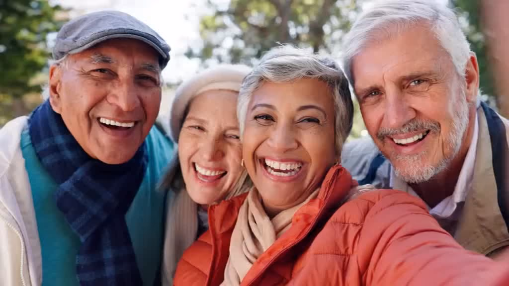Four smiling retirees taking a selfie together outdoors.