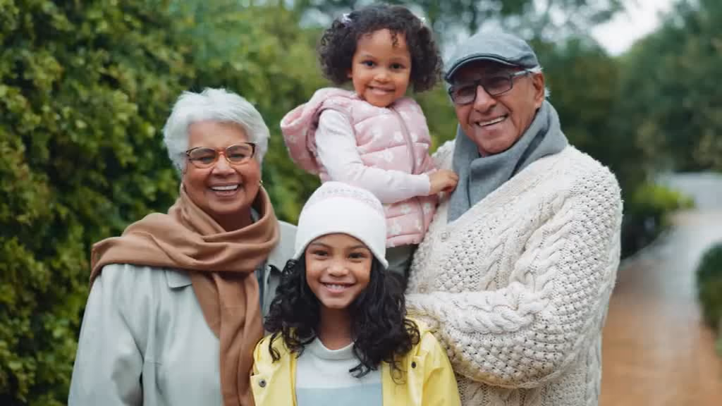 Grandparents outdoors with their two smiling granddaughters.
