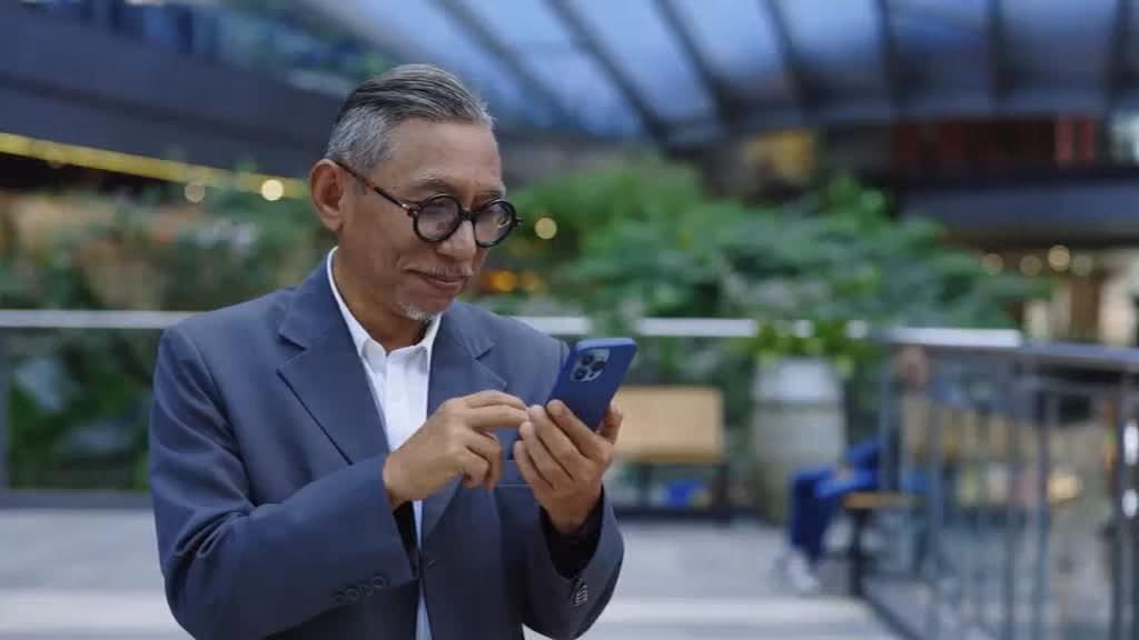 A man in a suit checking his phone outside an office building.